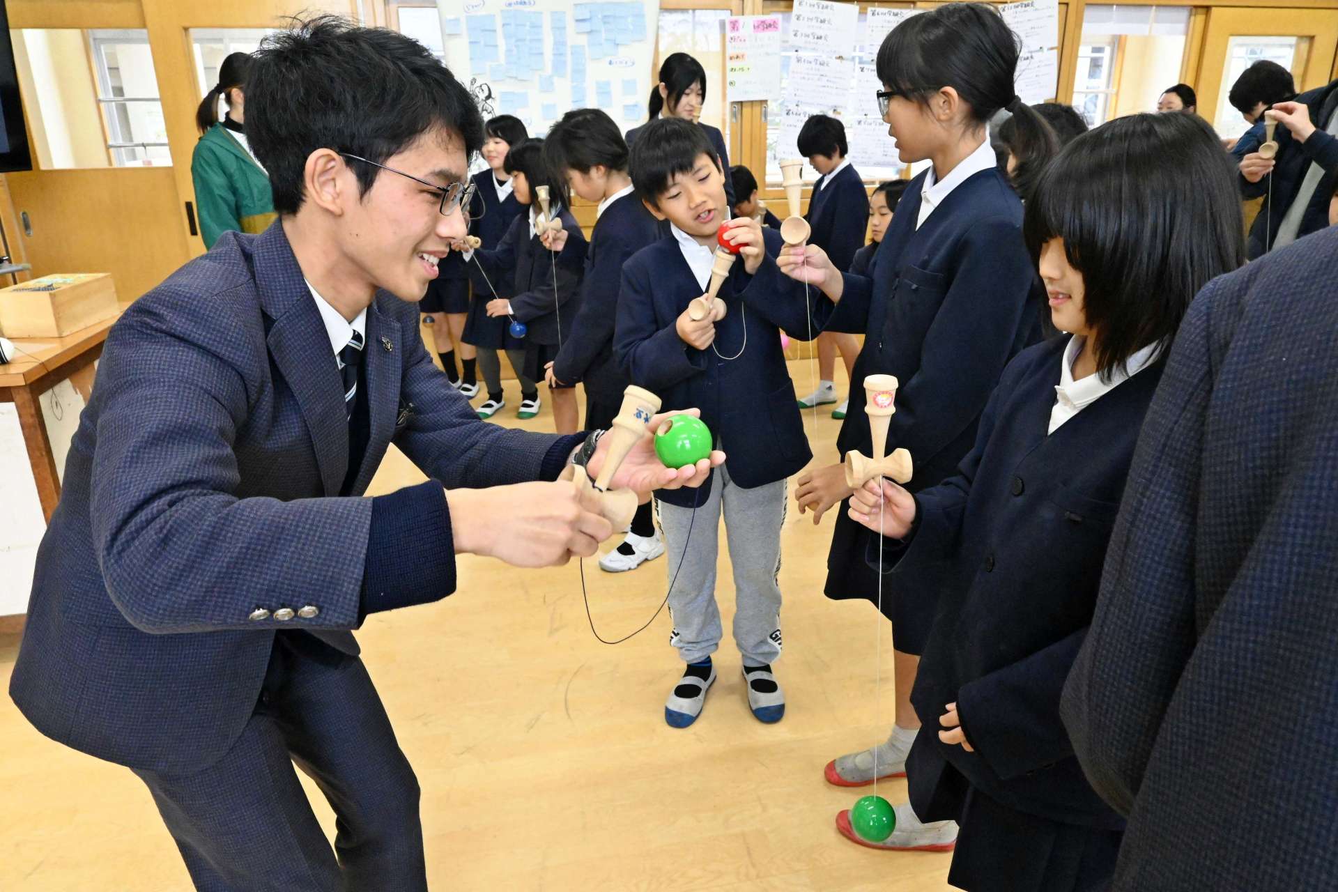 けん玉の基本を児童に教える葛賢伸さん（左）＝出水市の野田小学校