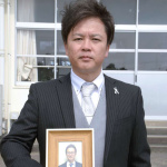 鳥越智巳さんの遺影を手にするＰＴＡ会長の今奈良孝さん＝１２日、指宿市の北指宿中学校