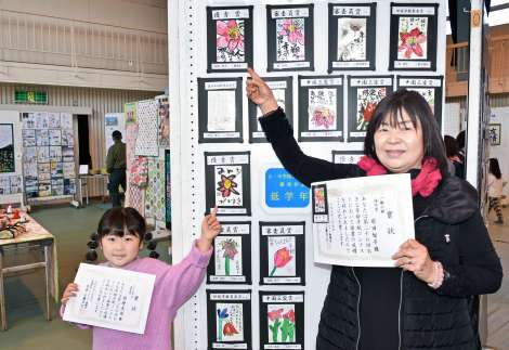 〈関連〉優秀賞を受賞した作品をそれぞれ指さす前田智子さん（右）と孫の原野美怜ちゃん＝伊佐市の本城小学校体育館