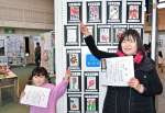 〈関連〉優秀賞を受賞した作品をそれぞれ指さす前田智子さん（右）と孫の原野美怜ちゃん＝伊佐市の本城小学校体育館
