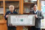 戦前の校歌の歌詞が載っている同窓会の寄贈品を手にする穂山睦男さん（左）と田崎小学校の岩戸淳校長＝鹿屋市の同校