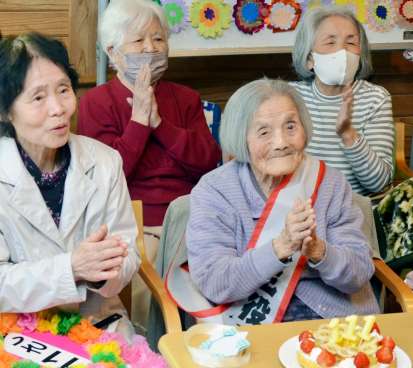 職員の出し物に笑顔で手拍子を送る坂下サトさん（前列右）。左は嫁の鈴子さん＝２０日、鹿児島市星ケ峯２丁目