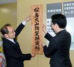 １日発足した「桜島火山防災研究所」の看板を掛ける井口正人所長（左）と下鶴隆央市長＝１日、鹿児島市役所