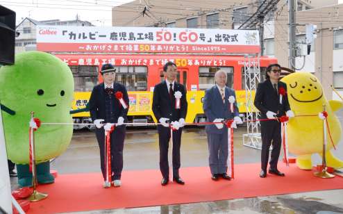 カルビー鹿児島工場操業５０周年を記念したラッピング電車の出発を祝う、久保進工場長（左から２人目）ら＝１日、鹿児島市交通局