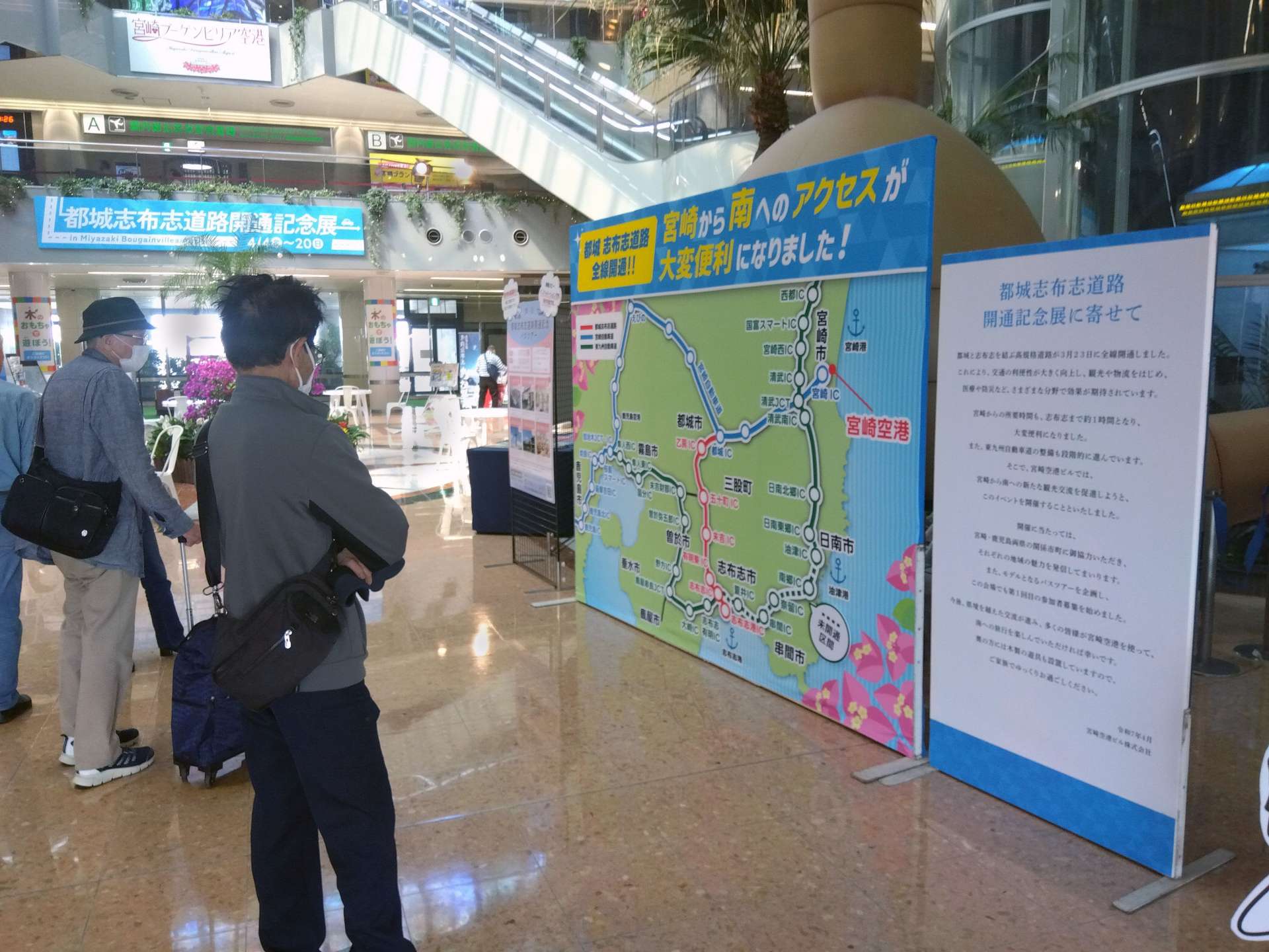 都城志布志道路の展示に見入る利用客＝４日、宮崎市赤江の宮崎空港