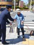 パッケージに標語が記されたパンを通行人に配る警察官（左）＝７日、鹿児島市鴨池新町