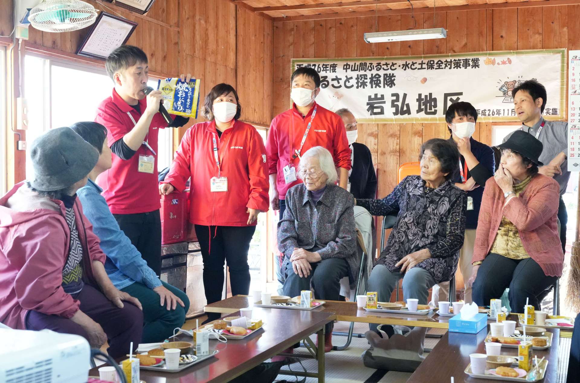 公民館への配達について、生協コープかごしまの職員から説明をうける高齢者ら＝８日、東串良町岩弘の岩弘中区公民館