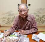 撮影した写真を手に、遺骨収集を振り返る野瀬純弘さん＝いちき串木野市金山下