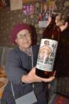 ６０周年記念ラベルの焼酎を持つ古閑妙子ママ＝１６日夜、伊佐市大口上町