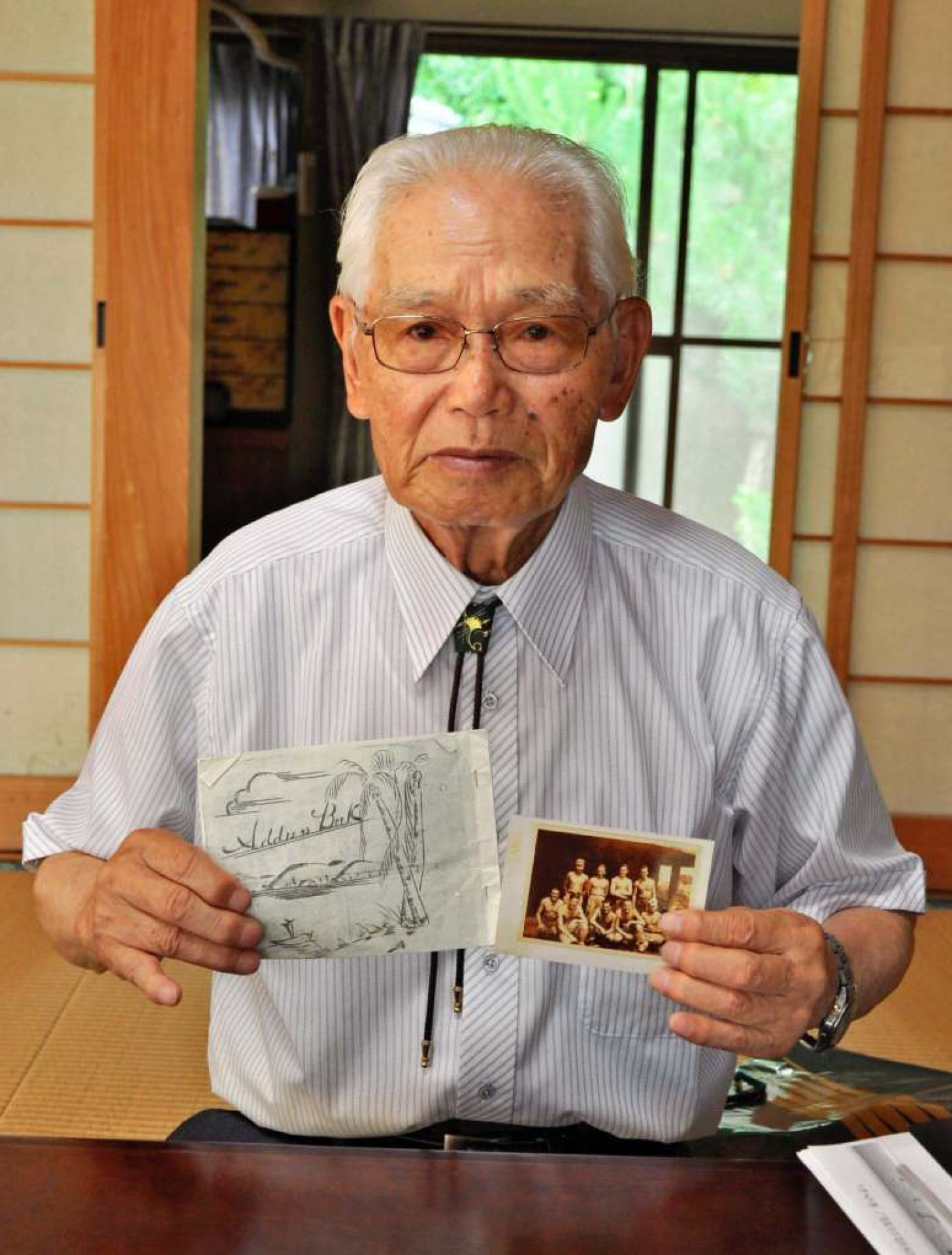 当時の写真などを手に体験を語る宇都口栄市さん＝出水市上鯖渕