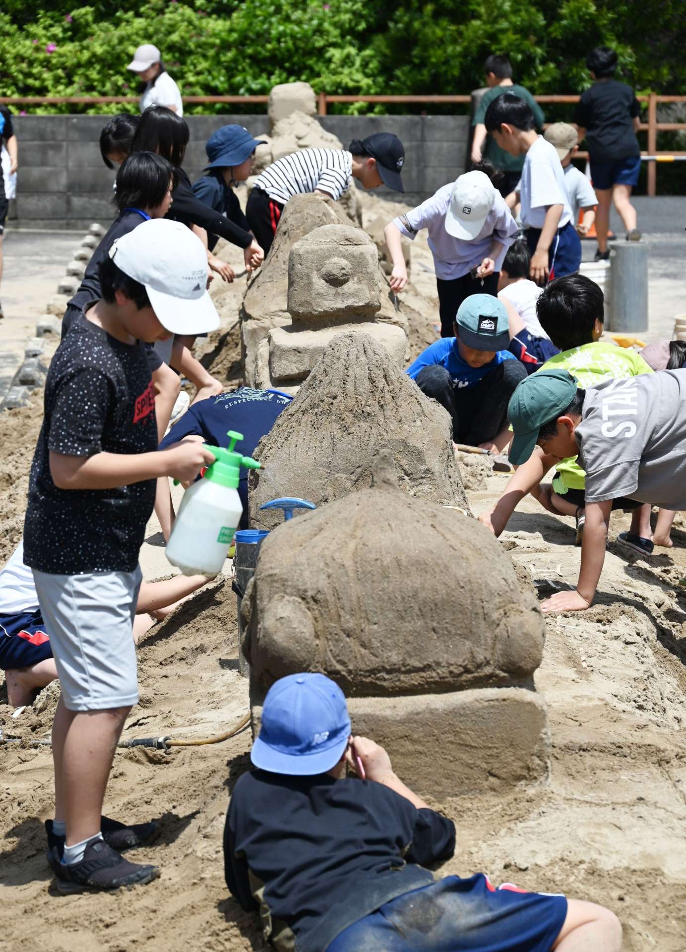 腹ばいになって砂の彫刻に挑む子どもたち＝１９日、南さつま市加世田麓町