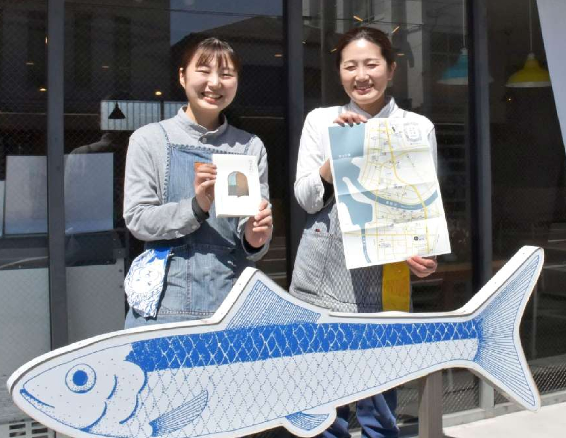 完成したガイド本と地図を手にする松出莉子さん（左）と泉野由起さん＝阿久根市鶴見町のイワシビル