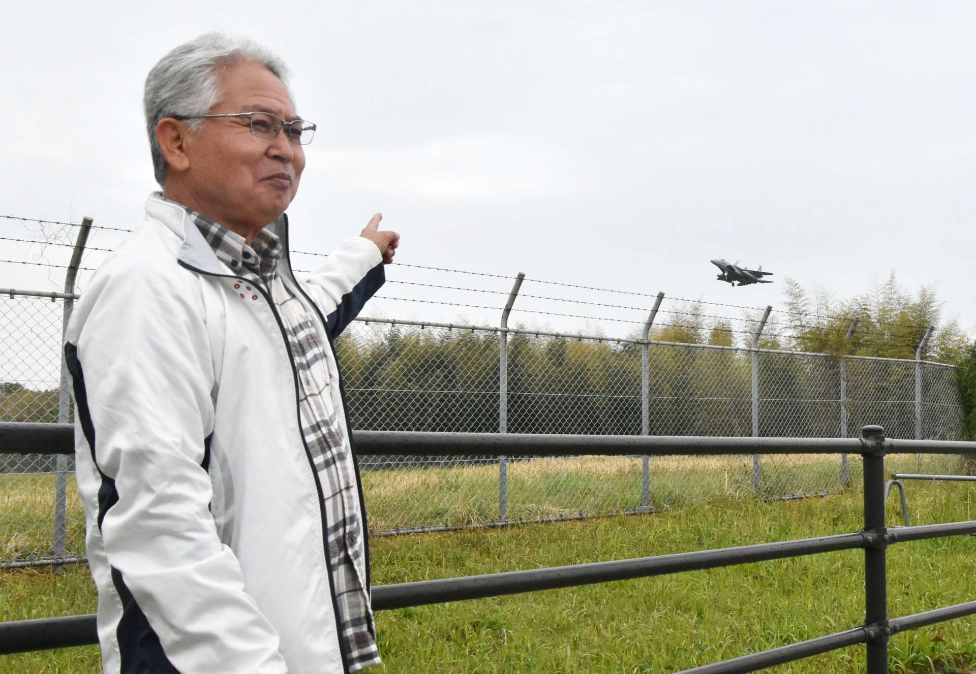 着陸しようとする新田原基地のＦ１５戦闘機を指さす海老原司さん＝１０日午後１時１５分ごろ、宮崎県新富町
