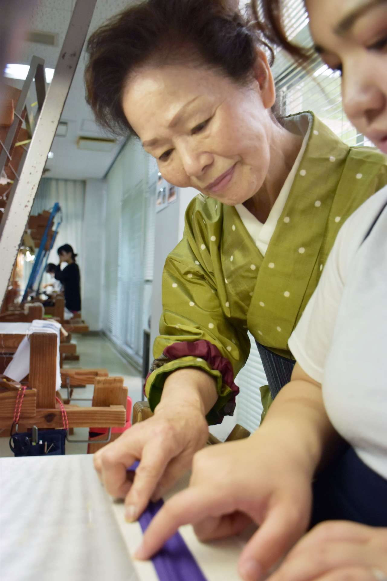 生徒に大島紬の織り方を指導する榮夏代さん＝奄美市