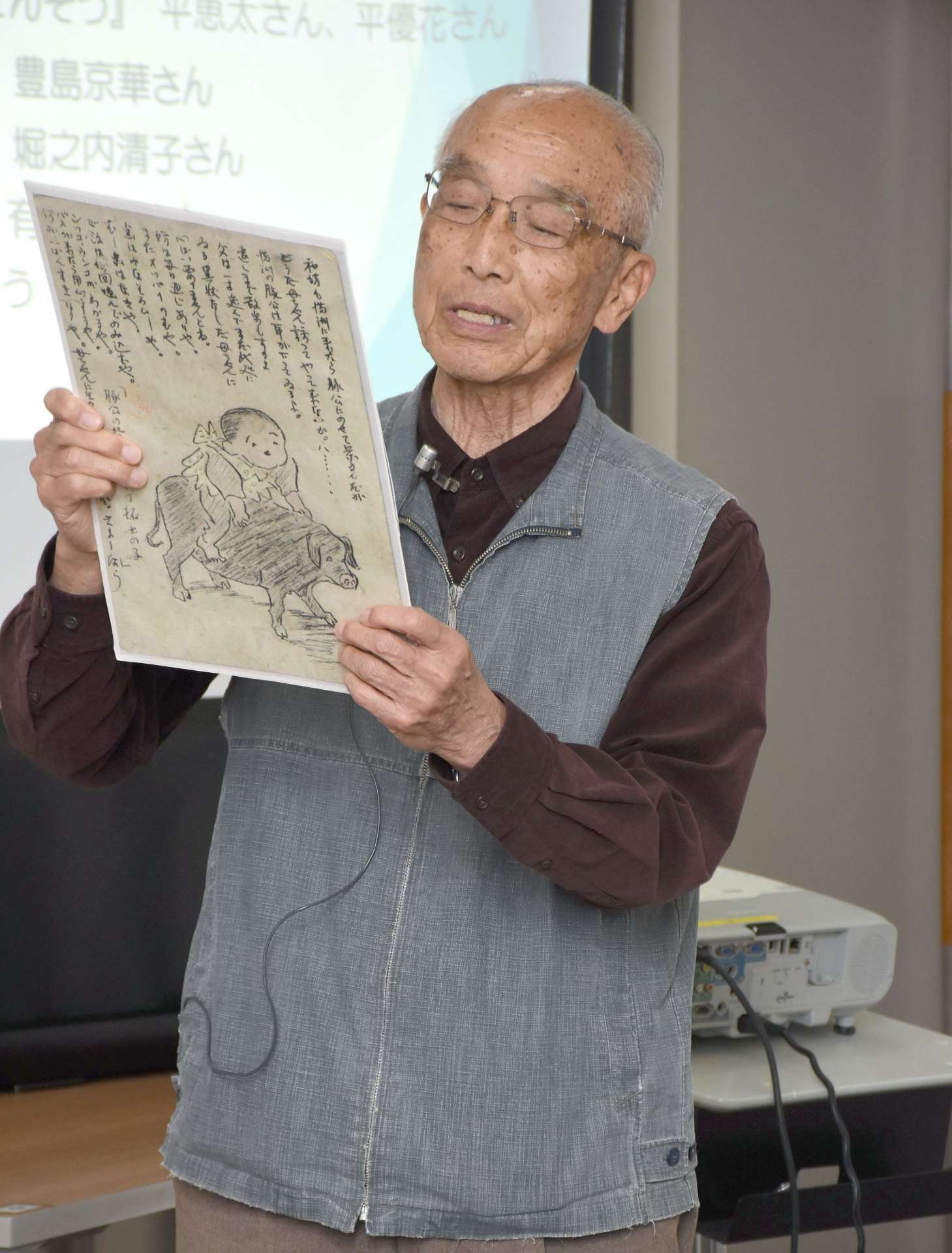 戦地にいる父親から送られてきた絵はがきについて紹介する有川和秀さん＝２７日、霧島市のメディアセンター