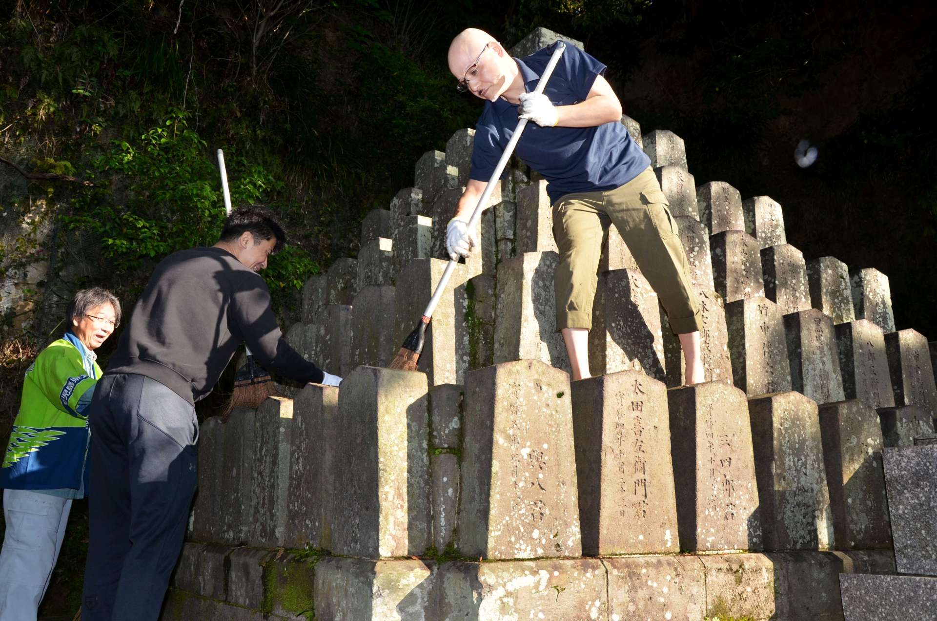 薩摩義士碑をほうきで掃いてきれいにする参加者＝２９日、鹿児島市城山町
