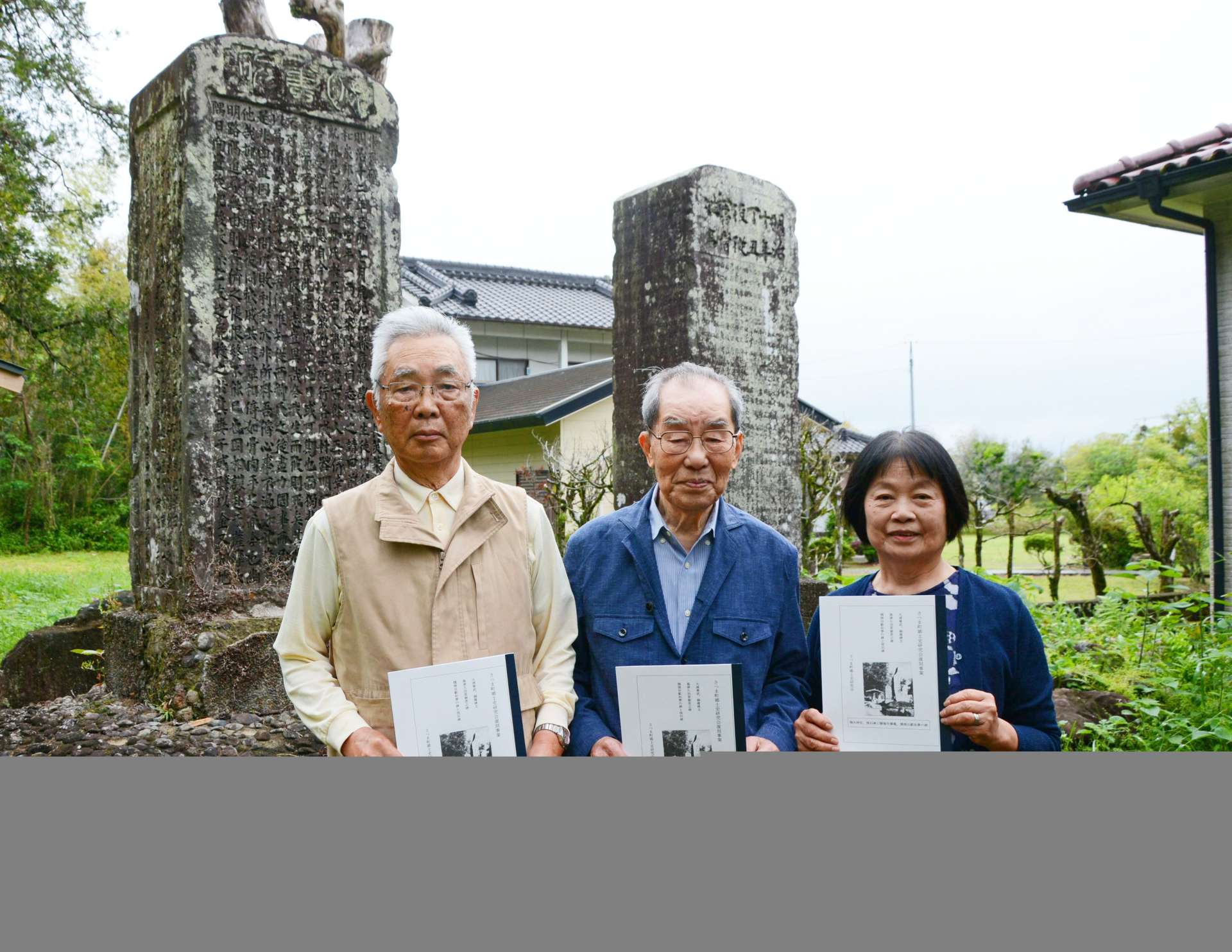 「悵旧碑」の前で冊子を手にするさつま町郷土史研究会復刻委員会のメンバーら＝さつま町宮之城屋地