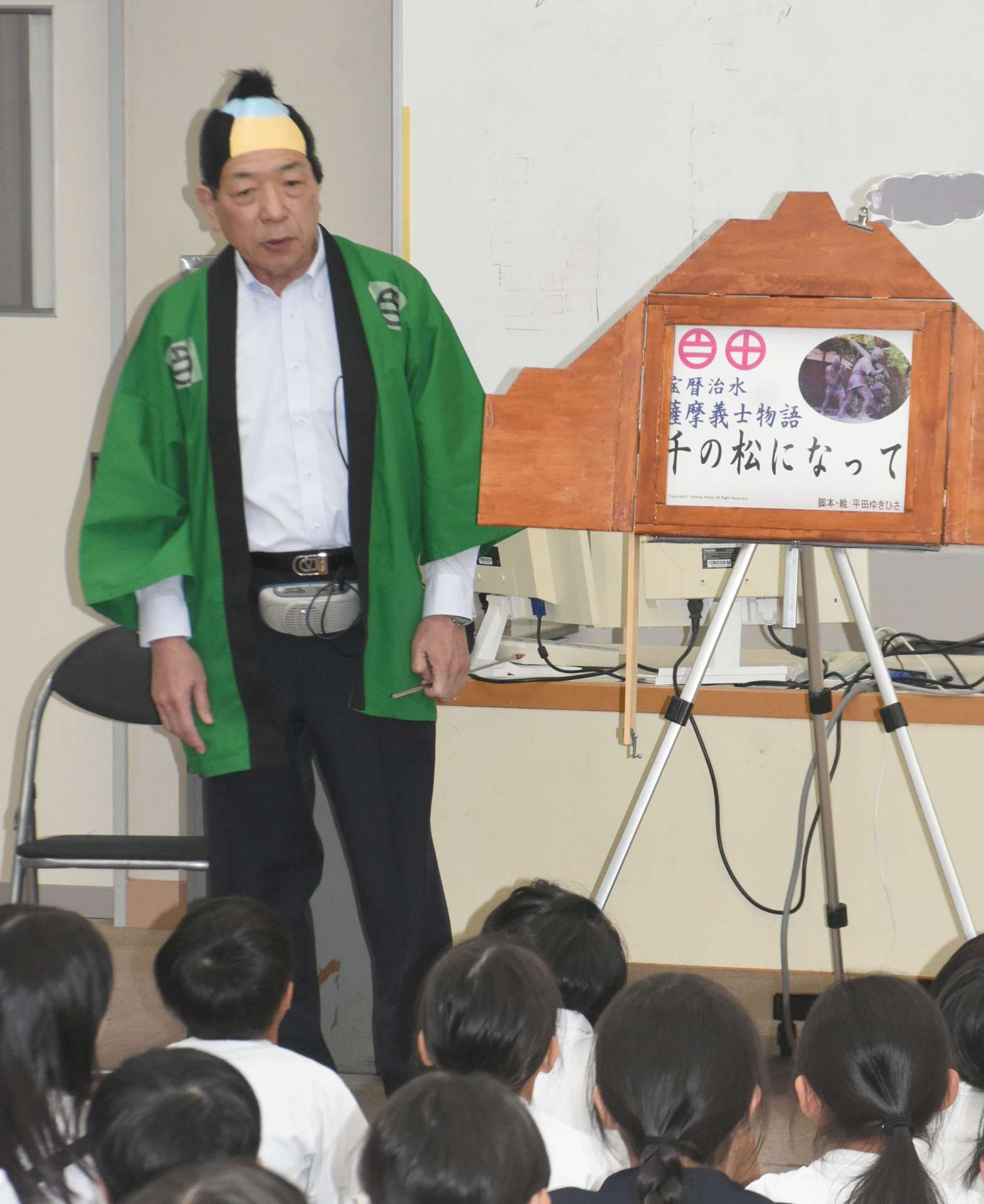 紙芝居で「宝暦治水」を伝える平田靱久さん＝鹿屋市の寿小学校