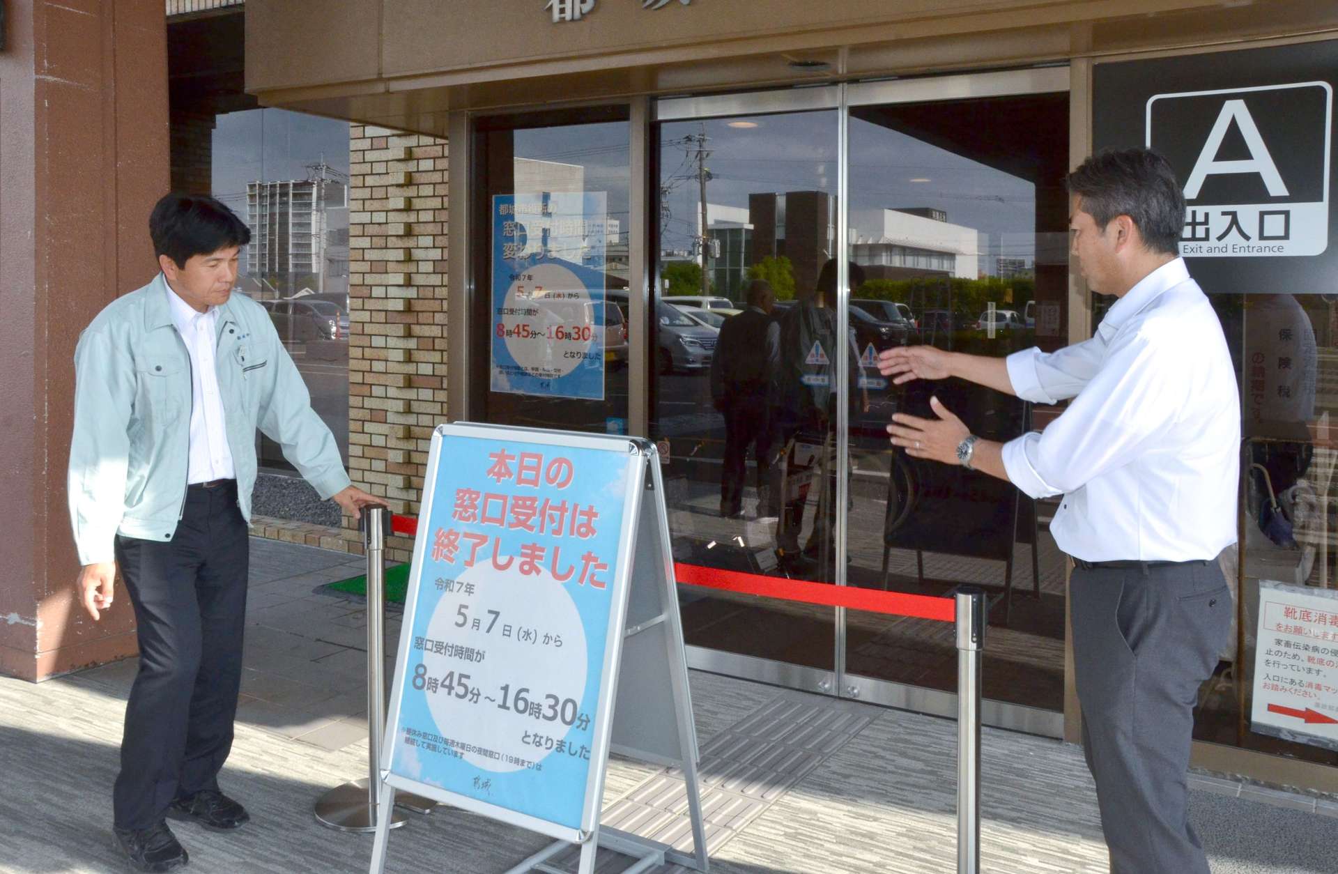 午後４時半に合わせ、都城市役所入り口に窓口受け付け終了の案内板を立てる職員＝７日、都城市姫城町