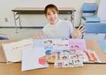 販売中のコラボグッズを広げて笑顔を見せる迫田さおりさん（スポーツビズ提供）