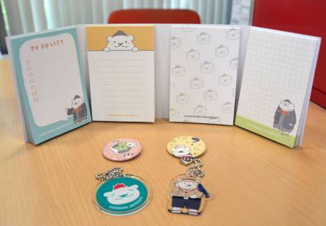 〈開発者の推しグッズ〉大学の公式キャラクター「さっつん」をあしらったパタパタメモや、ガチャガチャのカプセルに入っているのキーホルダーと缶バッジ