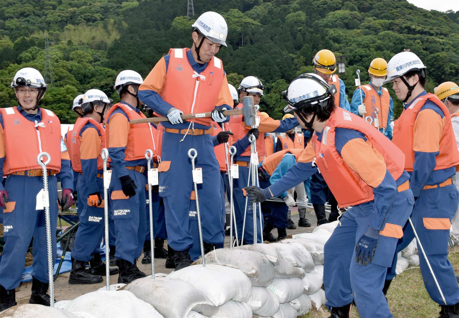 積み上げた土のうをくいで固定する消防団員ら＝薩摩川内市の川内川左岸河川敷