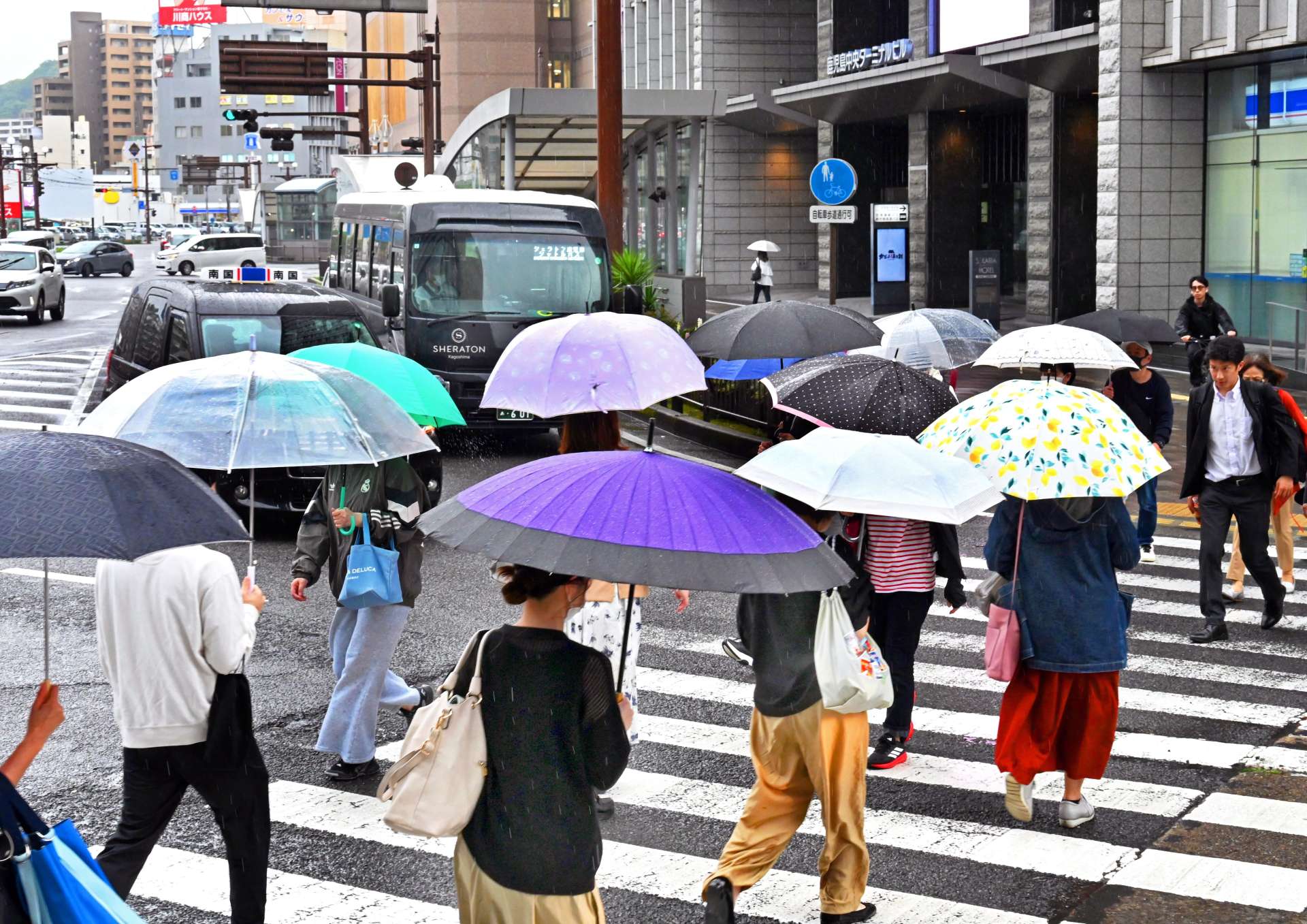 傘を差して、足早に交差点を渡る人たち＝１６日午後４時４０分、鹿児島市中央町