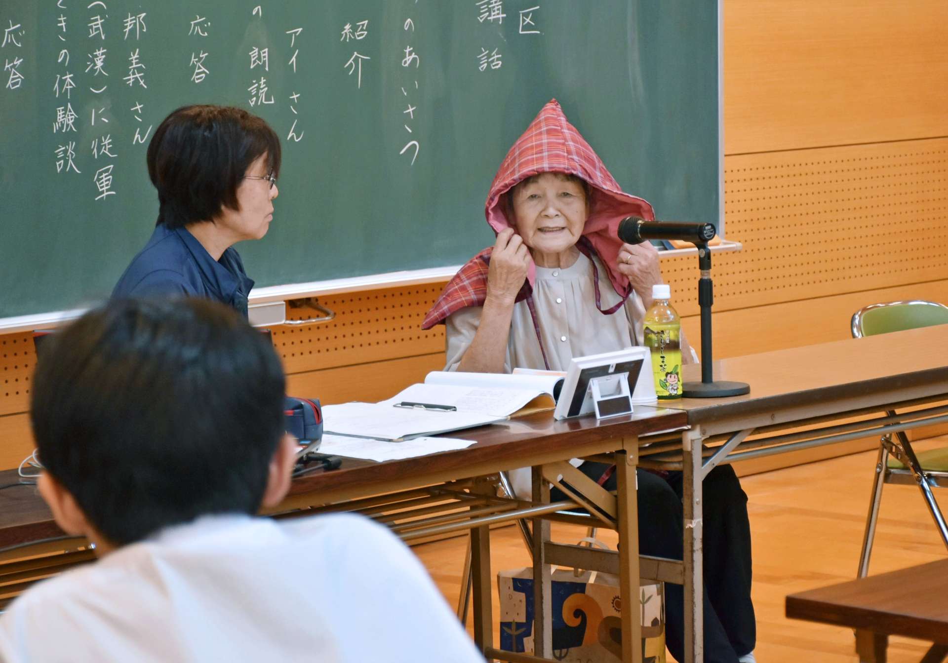 防空ずきんをかぶり、戦時中の体験を語る宮原アイさん＝２３日、霧島市の牧園中学校