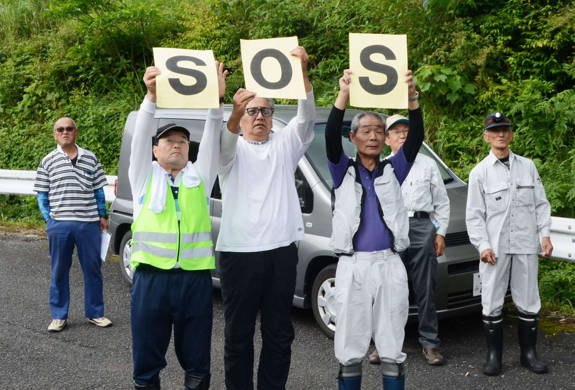 ドローンに向かって「ＳＯＳ」のボードを掲げる薬師集落の住民＝２５日、さつま町永野