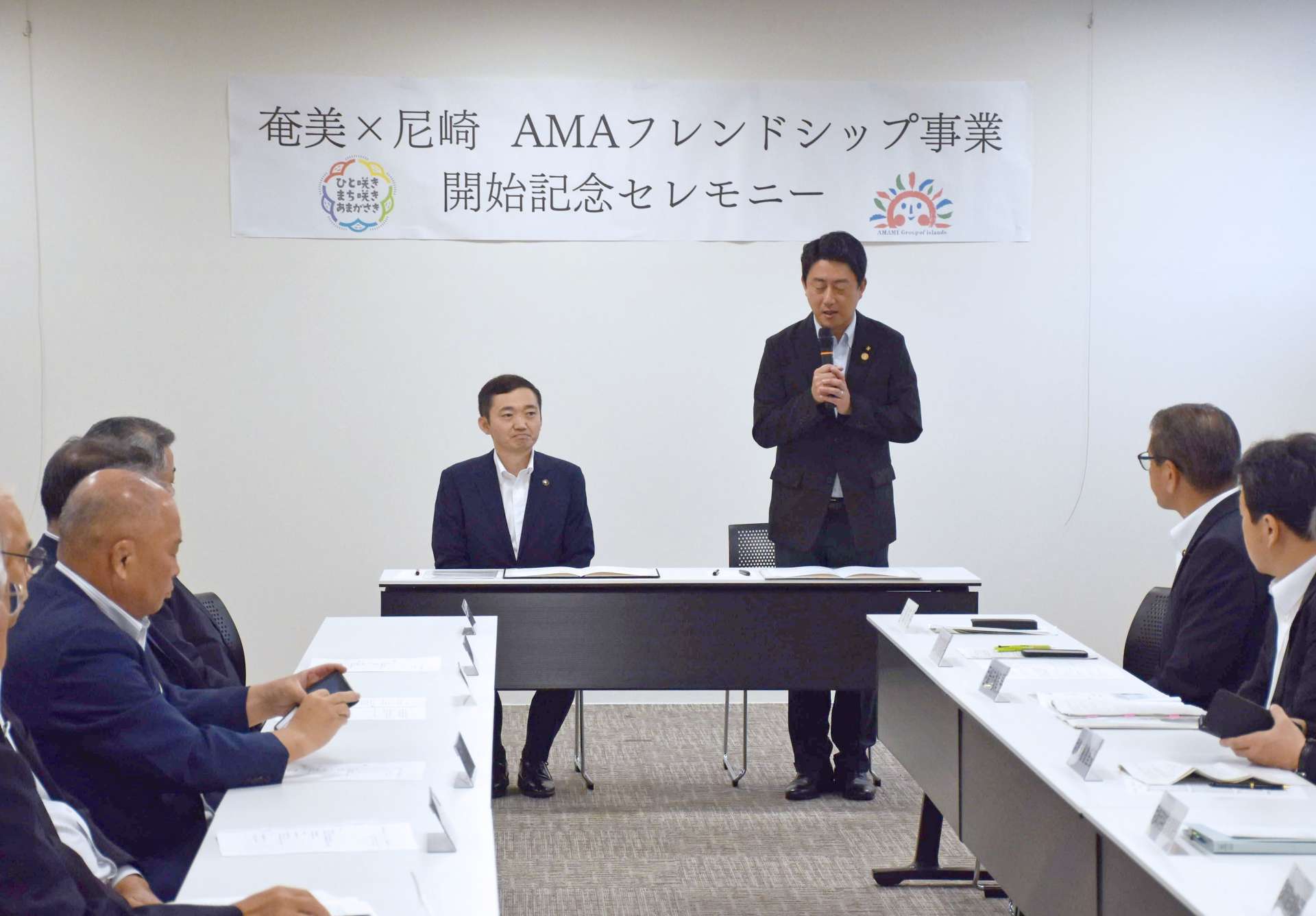 奄美群島の１２市町村の首長らが出席して開かれた締結式であいさつする松本眞尼崎市長（中央右）＝２６日、奄美市のアマホームＰＬＡＺＡ