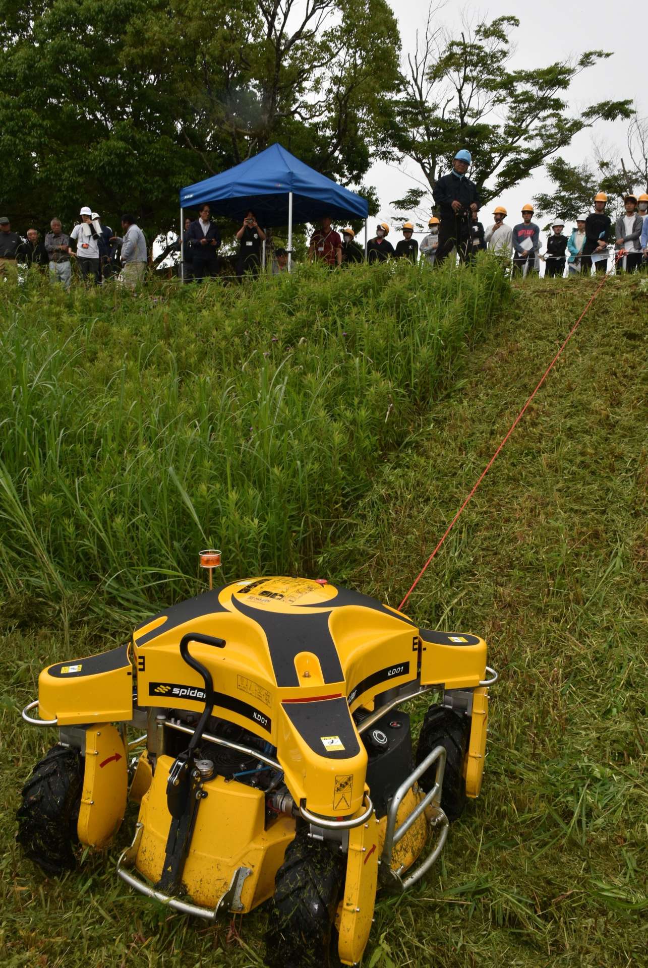 急斜面で作業するラジコン式草刈り機を見学する鹿児島大学の学生ら＝伊佐市大口里