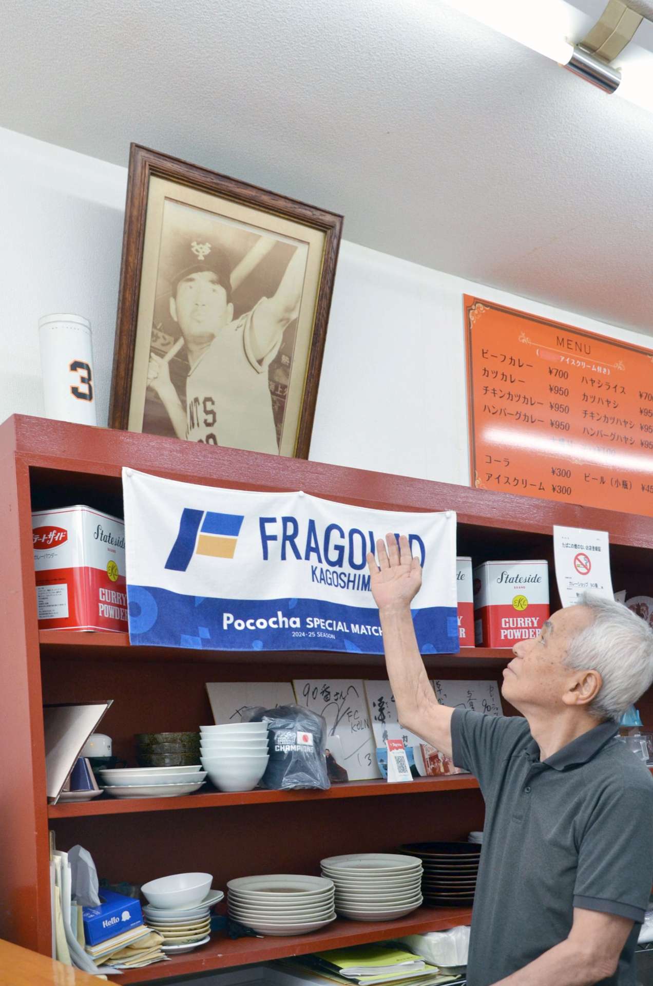 店内にある長嶋茂雄さんの写真を指し示す「カレーショップ９０番」の岩切秀史店長＝３日午後２時４５分ごろ、鹿児島市中央町