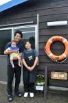 自分たちで建てた水産加工店の前に立つ池添慧さん、晴香さん夫妻と青ちゃん