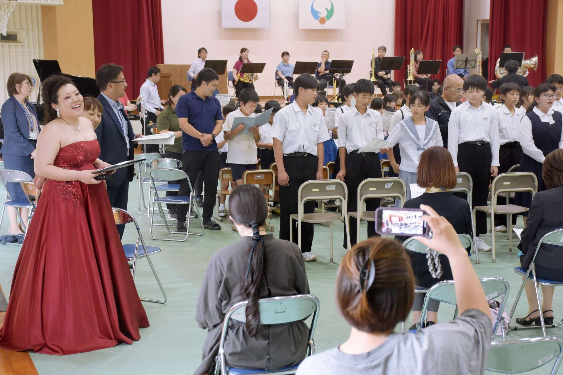 鹿児島交響楽団の演奏に合わせ、隈元奈津希さん（左）と「花は咲く」を歌う児童生徒＝志布志市の伊崎田小体育館