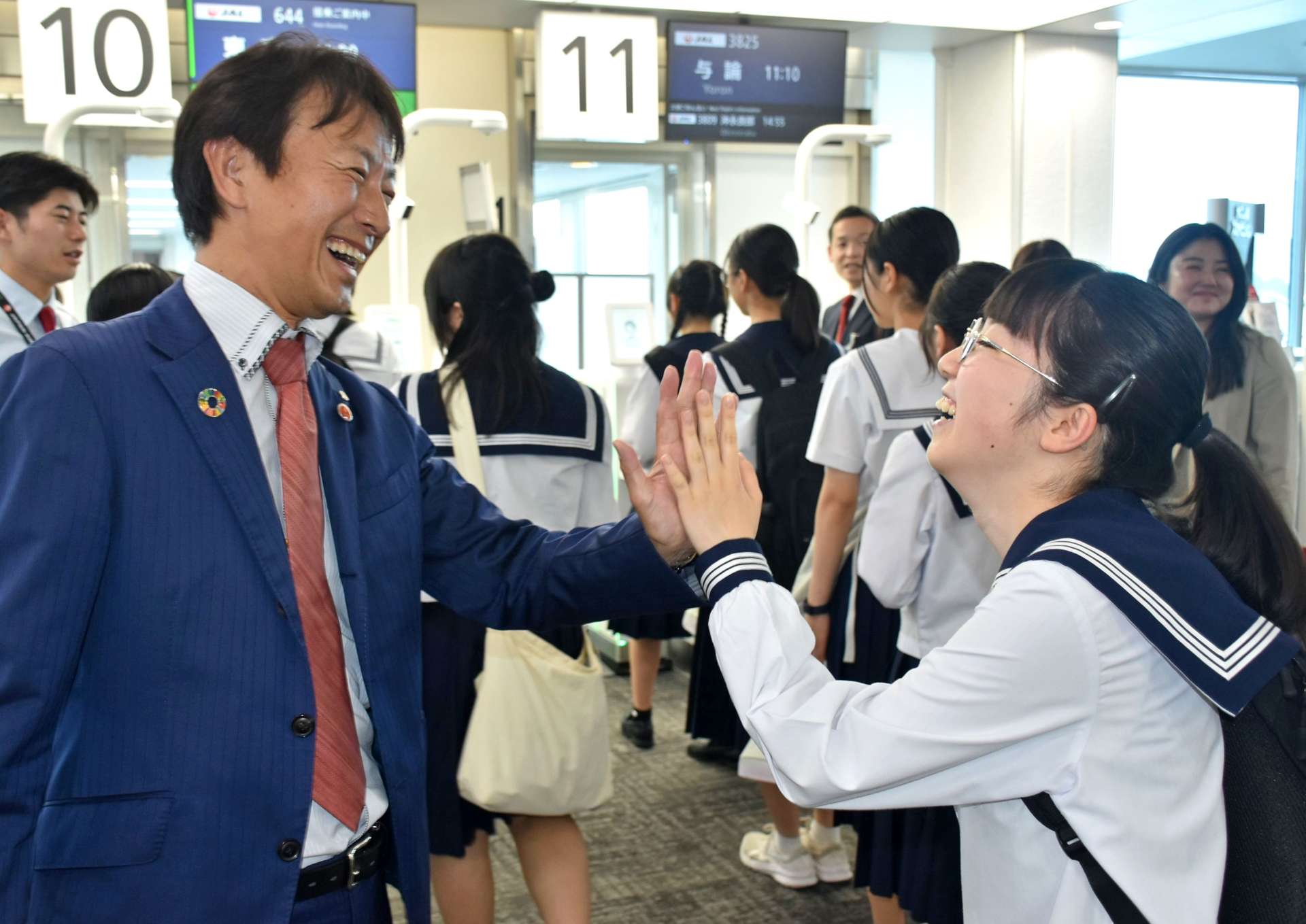 搭乗前にＪＡＬ鹿児島支店の中山洋彦支店長（左）とハイタッチをする甲南高校の生徒＝１０日、霧島市の鹿児島空港