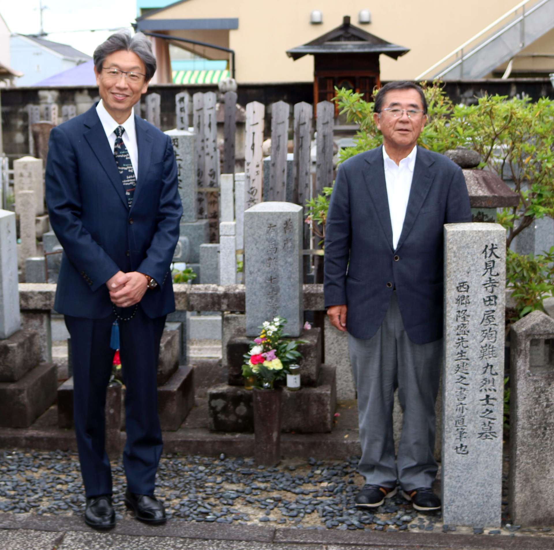 有馬新七の墓前に立つ坂木洋文さん（右）と齋藤透さん＝京都市伏見区の大黒寺