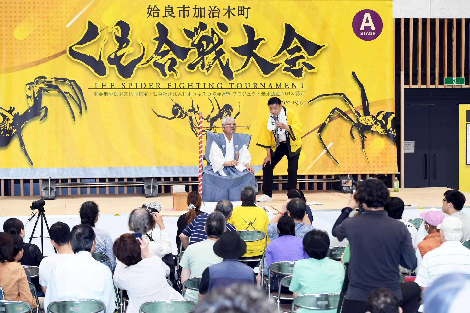 舞台上のくもに視線を注ぐ見物客＝１５日、姶良市役所加治木支所