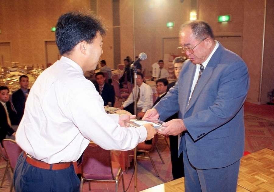 〈資料写真〉「定年祝う会」で教え子から記念の盾を受け取る塩瀬さん（右）＝１９９９年７月、鹿児島市