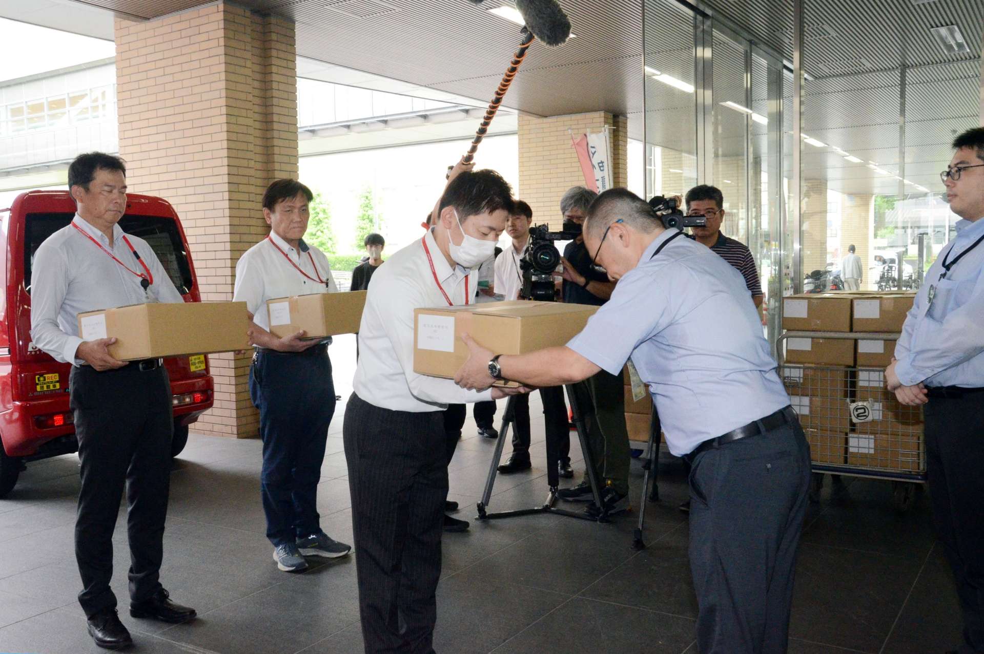 投票所整理券が入った箱を山森竜彦市選管事務局長（右から２人目）から受け取る郵便局の担当者＝２６日、鹿児島市役所