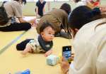 赤ちゃんの一瞬の表情を捉えようと奮闘する参加者＝３日、鹿児島市東部親子つどいの広場なかまっち