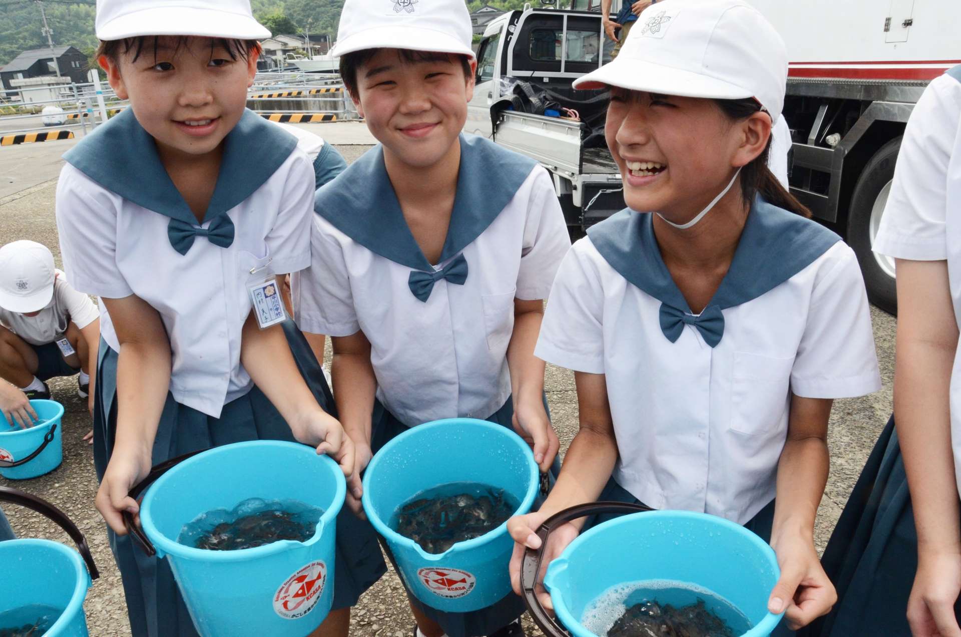 マダイの稚魚が入ったバケツを手にする平川小学校の児童＝４日、鹿児島市平川町の平川ヨットハーバー