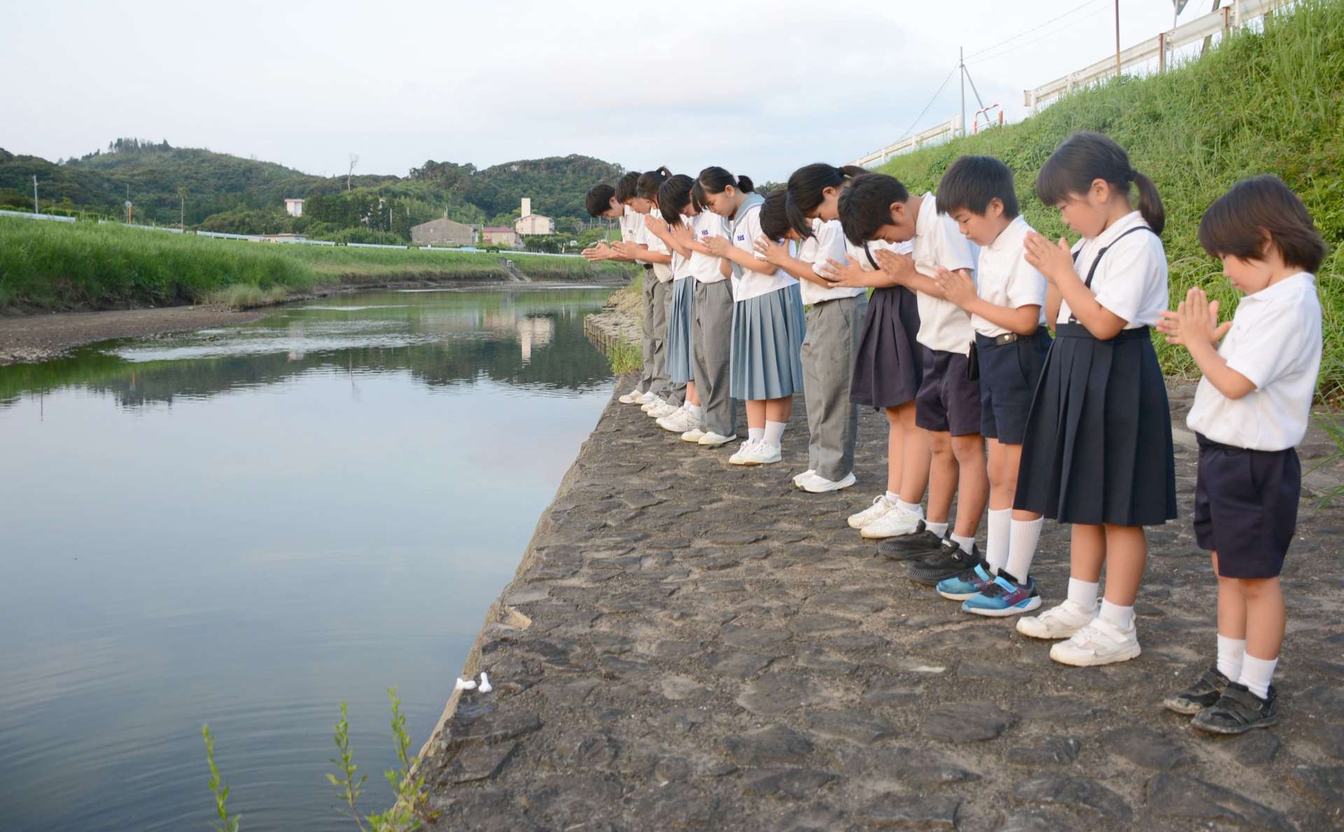 花渡川に向かって手を合わせる小中学生＝枕崎市鹿篭麓町