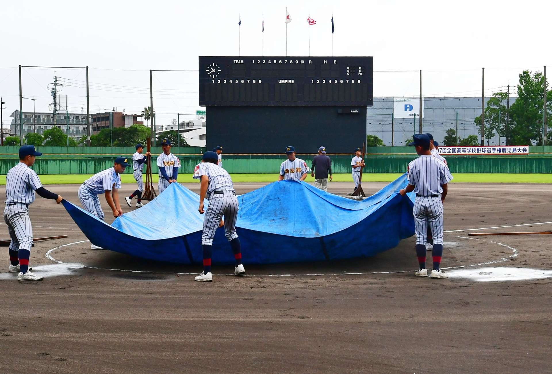 雨天順延が決まりグラウンドで作業をする選手ら＝１３日午前、鹿児島市の鴨池市民球場