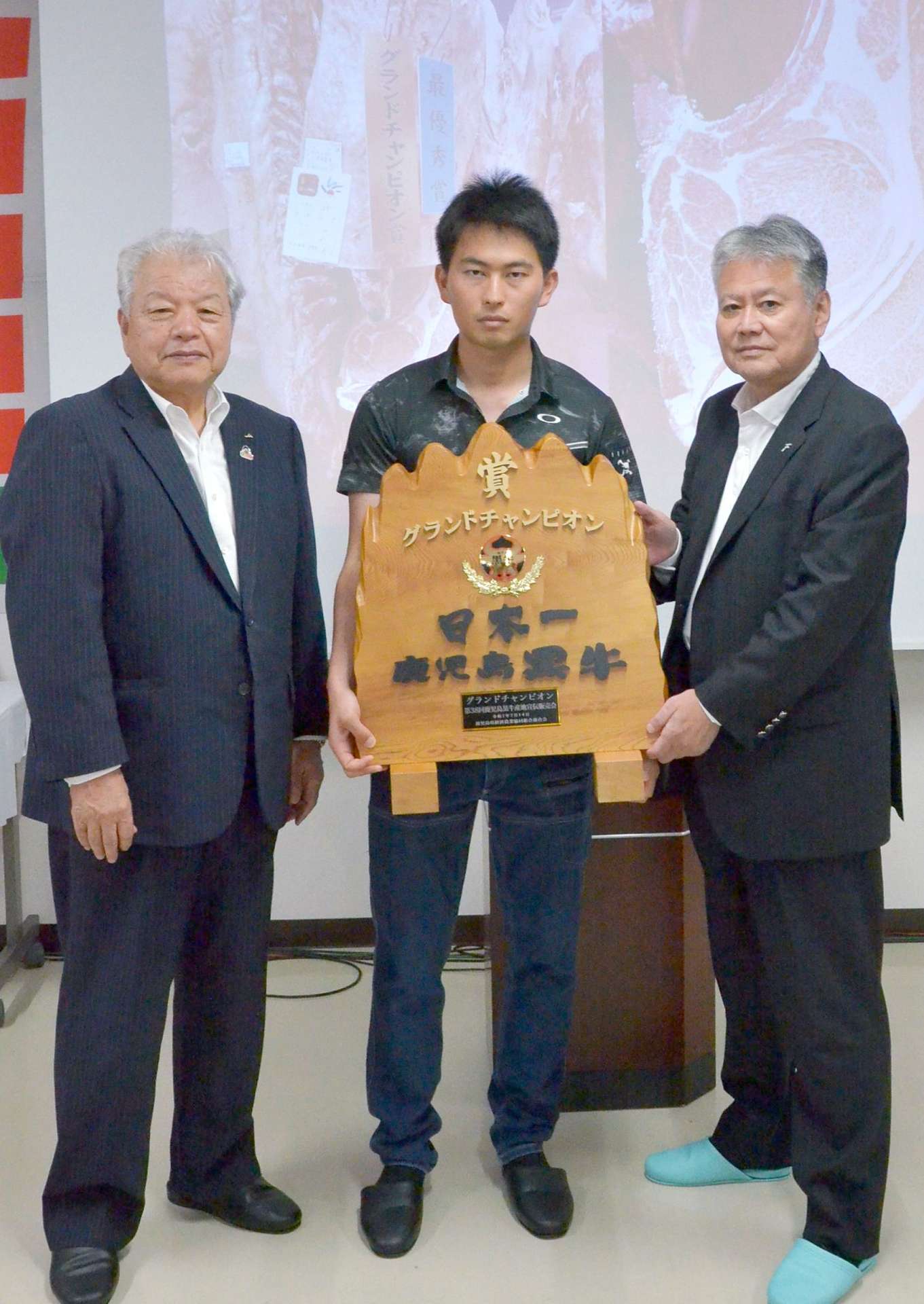 グランドチャンピオンに選ばれた薬師成人さんの息子の大志さん（中央）＝１４日、南九州市のＪＡ食肉かごしま南薩工場