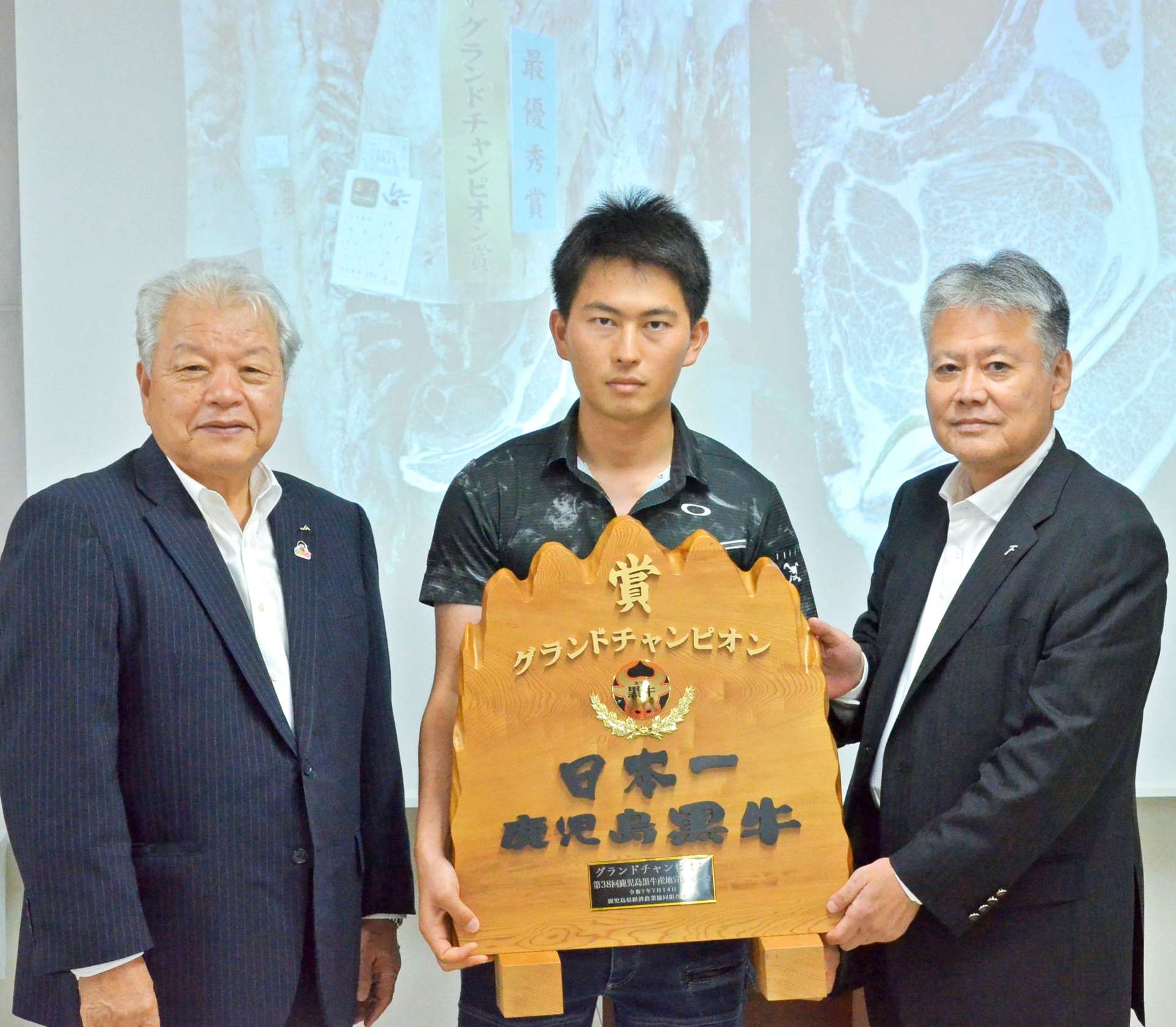 グランドチャンピオンに選ばれた薬師成人さんの息子の大志さん（中央）＝１４日、南九州市のＪＡ食肉かごしま南薩工場