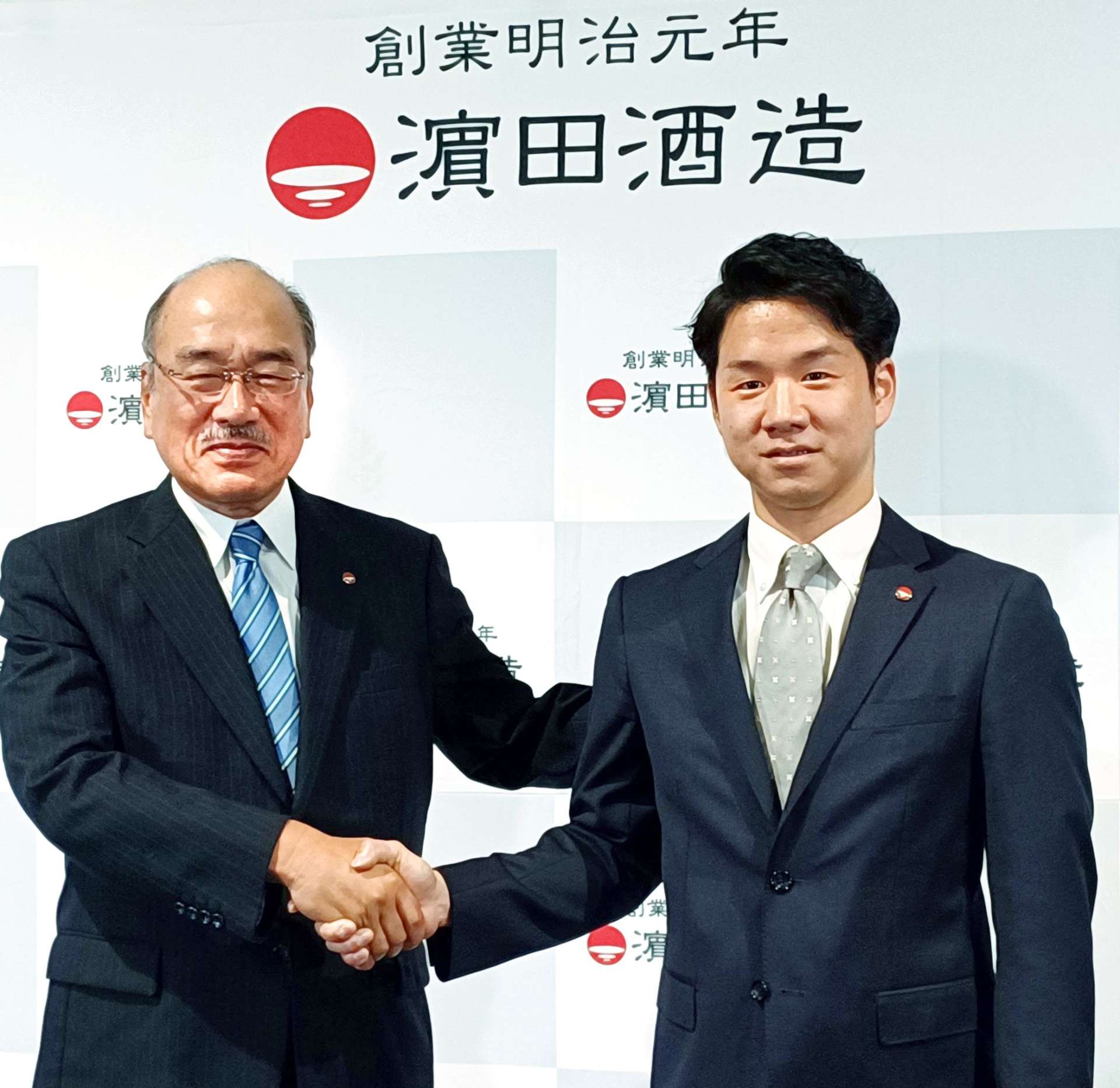 社長交代の会見後に握手する浜田雄一郎さんと浜田光太郎さん（右）＝１４日、いちき串木野市の浜田酒造
