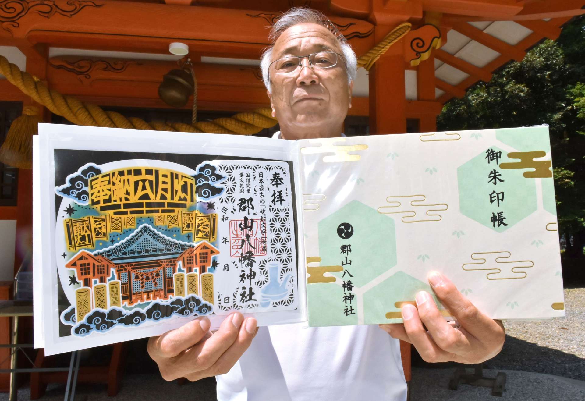 初の３色刷りで六月灯をテーマにした切り絵御朱印と御朱印帳を持つ山下和弘氏子総代表＝伊佐市の郡山八幡神社