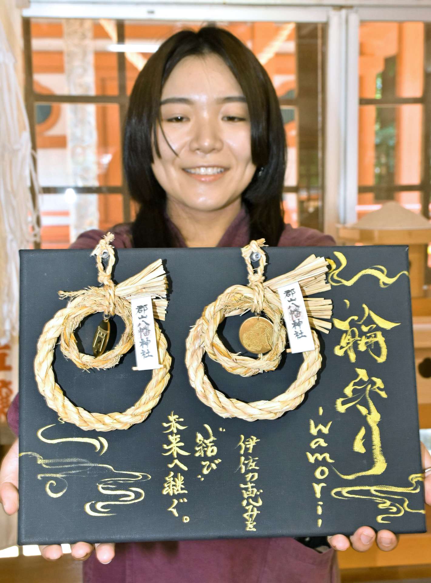 予約販売する「輪守り」を持つ和繼の井料明歩代表＝伊佐市の郡山八幡神社