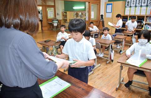 担任教諭から通知表を受け取る児童＝１８日、霧島市牧園町高千穂の高千穂小学校