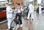 ヘルメットのあごひもを締めるよう生徒に指導する警察官＝１４日午前８時前、鹿児島市西田３丁目